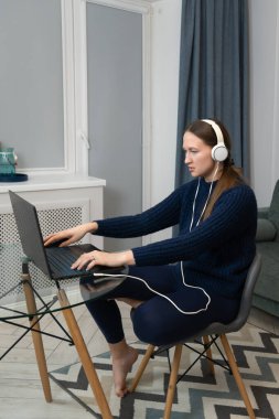 Kulaklık takan ve cam bir masada çıplak ayakla oturan genç bir kadın rahat bir oturma odasında dizüstü bilgisayarını yazarken uzaktan kumandalı işine konsantre oluyor. Dikey fotoğraf