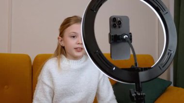 Genç nüfuzlu kişi, parlak sarı koltukta otururken video blogu kaydediyor. Profesyonel içerik yaratmak için akıllı telefon ve halka ışığını kullanıyor.