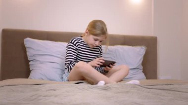 Rahat bir şekilde yatakta uzanırken kendini mobil oyunlara kaptıran genç bir kız, rahat ev ortamında dijital eğlenceyle derinden meşgul.