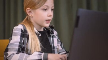 Hevesli bir ilkokul öğrencisi kodlama becerileri geliştirir, ahşap bir masada özenle dizüstü bilgisayarda yazar, teknoloji eğitimindeki odak ve kararlılığını gösterir.