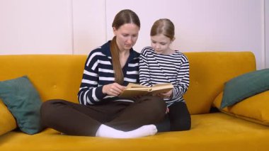 Annem kızına kitap okuyor. Oturma odalarındaki sarı bir kanepede rahat rahat otururken rahat ve eğitici bir ortam yaratıyor.