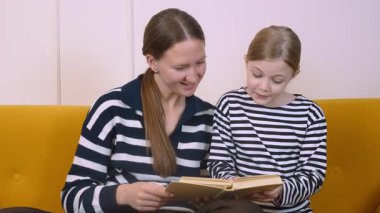 Annem kızına kitap okuyor. Oturma odalarındaki sarı bir kanepede rahat rahat otururken rahat ve eğitici bir ortam yaratıyor.