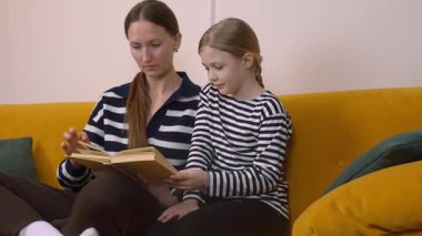 Annem, küçük kızına kitap okumasında yardım ediyor. Oturma odasındaki rahat sarı kanepede birlikte otururken kelimelere ve anlamlarına işaret ediyor.