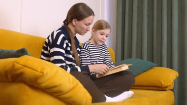 Annem, küçük kızına kitap okumasında yardım ediyor. Oturma odasındaki rahat sarı kanepede birlikte otururken kelimelere ve anlamlarına işaret ediyor.