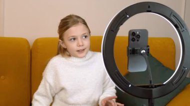 Hevesli genç kız çevrimiçi içerik yaratıyor, rahat bir koltukta otururken seyircilerle yakınlaşıyor, en uygun ışıklandırma için halka ışığını kullanıyor.