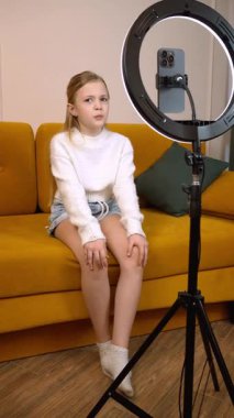 Beyaz kazaklı genç bir kız akıllı telefonuyla, sanki bir vlog ya da diğer çevrimiçi içerik dikey video kaydediyormuş gibi iletişim halinde.