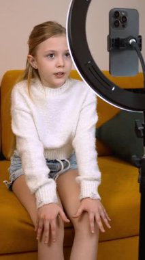 Beyaz kazaklı genç bir kız akıllı telefonuyla, sanki bir vlog ya da diğer çevrimiçi içerik dikey video kaydediyormuş gibi iletişim halinde.