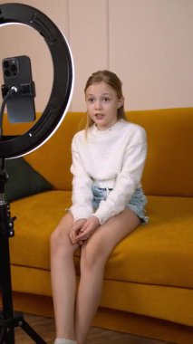 Genç bayan yaratıcı akıllı telefon ve halka ışığı kullanarak video içeriği kaydediyor, sosyal medya materyali dikey video üretirken çok yönlü ifadeler ve dinamik kamera açıları gösteriyor