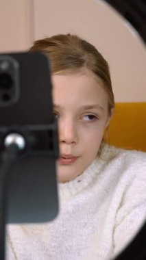 Genç bayan yaratıcı akıllı telefon ve halka ışığı kullanarak video içeriği kaydediyor, sosyal medya materyali dikey video üretirken çok yönlü ifadeler ve dinamik kamera açıları gösteriyor