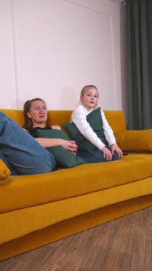 Sıcak aile anları, anne ve kızının sarı koltukta oturup film izlediğini ve dikey entrika üzerine animasyon sohbetleri yaptığını gösteriyor.