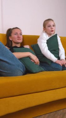 Sıcak aile anları, anne ve kızının sarı koltukta oturup film izlediğini ve dikey entrika üzerine animasyon sohbetleri yaptığını gösteriyor.