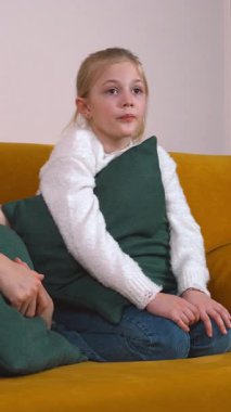 Sıcak aile anları, anne ve kızının sarı koltukta oturup film izlediğini ve dikey entrika üzerine animasyon sohbetleri yaptığını gösteriyor.