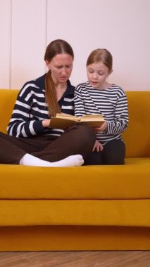 Anne, küçük kızının okumayı öğrenmesine yardım ediyor. Oturma odalarındaki hardal renkli koltukta rahatça oturup sıcak ve eğitici bir bağ kurma deneyimi yaratıyor.