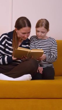 Anne, küçük kızının okumayı öğrenmesine yardım ediyor. Oturma odalarındaki hardal renkli koltukta rahatça oturup sıcak ve eğitici bir bağ kurma deneyimi yaratıyor.