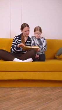 Anne, küçük kızının okumayı öğrenmesine yardım ediyor. Oturma odalarındaki hardal renkli koltukta rahatça oturup sıcak ve eğitici bir bağ kurma deneyimi yaratıyor.