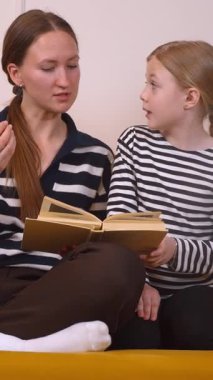 Anne, küçük kızının okumayı öğrenmesine yardım ediyor. Oturma odalarındaki hardal renkli koltukta rahatça oturup sıcak ve eğitici bir bağ kurma deneyimi yaratıyor.