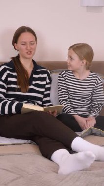 Genç okur yazarlığı beslemek, ilgili anne kızına rehberlik ederken yumuşak sarı koltukta birlikte okumak, rahat ev ortamında özel öğrenme deneyimini paylaşmak, dikey videolar.