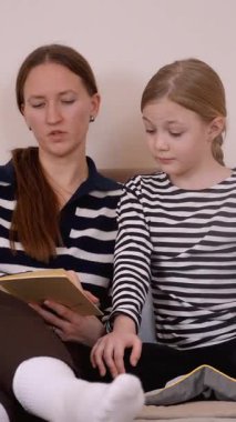 Anne çocuğuna bir kitap okuyor. Kanepede rahatça otururken çeşitli duygu ve ifadeleri gösteriyor. Dikey bir videonun değerli bir anını paylaşıyor.