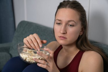 Kanepede rahat bir şekilde oturan genç kadın evde tek başına sıkıcı bir film izlerken cam kaseden patlamış mısır yiyordu. Sıkıntı ve yalnızlığın ağırlığını hissediyordu.