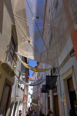 Coimbra, Portekiz - 15 Ağustos 2022: Sokak manzarası binalar ve sayısız turist arasında örülmüş gölgelerle dar bir sokak aralığı gösteriyor