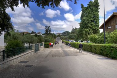 Fatima, Portekiz - 15 Ağustos 2022: Hareket halindeki ağaçlar ve çalıların bulunduğu erişim yolu bulanık turistler ve hacılar