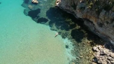 Yunanistan 'ın Alonissos adasındaki kayalık alanda yüzen turistlerin bulunduğu Chrisi Milia plajı üzerindeki hava manzarası.