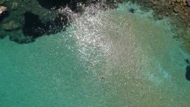 Yunanistan 'ın Alonissos adasındaki kayalık alanda yüzen turistlerin bulunduğu Chrisi Milia plajı üzerindeki hava manzarası.