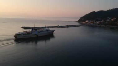 Scenic view of Anes Ferry boat docking in a small beautiful Greek harbor at sunset. The picturesque port of Glossa village in Skopelos island, Sporades, Greece. 