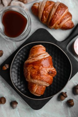 Çikolatalı çıtır kruvasan ve açık beton arka planda canlandırıcı bir fincan kahve. Lezzetli besleyici kahvaltı.