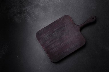 Ahşap kesme tahtası, mutfak aletleri ve siyah beton arka plan. Evde yemek pişirmek.