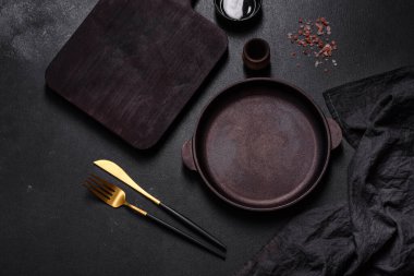 Koyu beton arka planda mutfak aletleri olan kahverengi demir tencere. Evde yemek pişirmek.