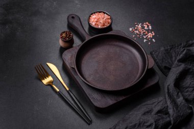 Koyu beton arka planda mutfak aletleri olan kahverengi demir tencere. Evde yemek pişirmek.