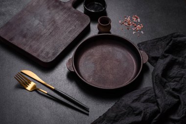 Koyu beton arka planda mutfak aletleri olan kahverengi demir tencere. Evde yemek pişirmek.