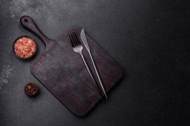 Ahşap kesme tahtası, mutfak aletleri ve siyah beton arka plan. Evde yemek pişirmek.