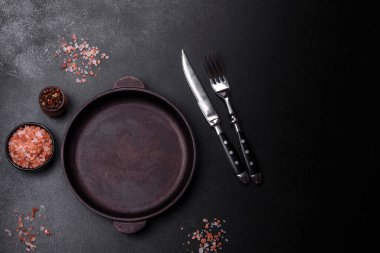 Koyu beton arka planda mutfak aletleri olan kahverengi demir tencere. Evde yemek pişirmek.