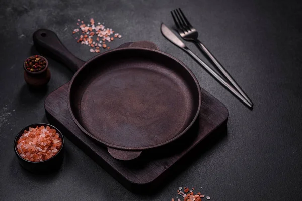 stock image Brown iron empty pan with kitchen utensils on a dark concrete background. Cooking at home