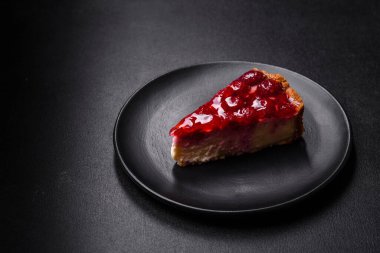 Ev yapımı lezzetli peynirli kek, jöle ve ahududu arkaplanda siyah bir tabakta.