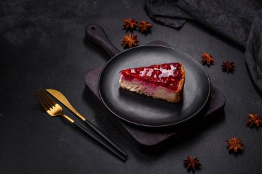 Ev yapımı lezzetli peynirli kek, jöle ve ahududu arkaplanda siyah bir tabakta.