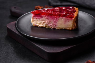 Ev yapımı lezzetli peynirli kek, jöle ve ahududu arkaplanda siyah bir tabakta.