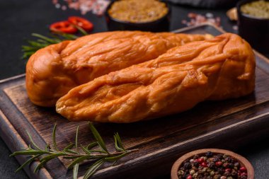 Lezzetli tütsülenmiş tavuk göğsü filetosu. Baharat ve otlarla birlikte. Koyu beton arka planda ahşap kesim tahtasının üzerinde.