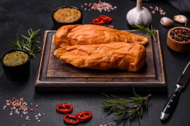 Lezzetli tütsülenmiş tavuk göğsü filetosu. Baharat ve otlarla birlikte. Koyu beton arka planda ahşap kesim tahtasının üzerinde.