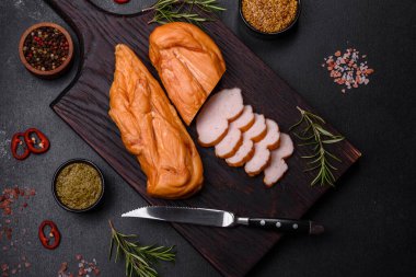 Lezzetli tütsülenmiş tavuk göğsü filetosu. Baharat ve otlarla birlikte. Koyu beton arka planda ahşap kesim tahtasının üzerinde.