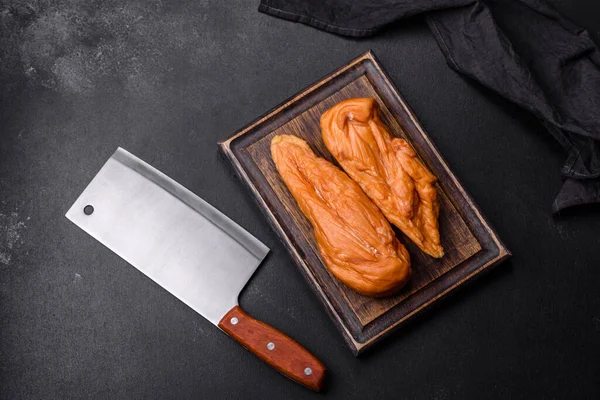 stock image Tasty smoked fillet of chicken breast with spices and herbs on a wooden cutting board on a dark concrete background