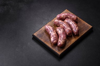 Koyu beton bir masada baharat ve otlarla ızgara yapılmış çiğ domuz sosisi. Evde yemek pişirmek.