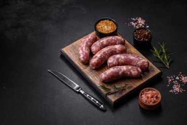 Koyu beton bir masada baharat ve otlarla ızgara yapılmış çiğ domuz sosisi. Evde yemek pişirmek.