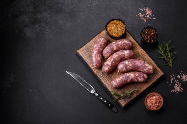 Koyu beton bir masada baharat ve otlarla ızgara yapılmış çiğ domuz sosisi. Evde yemek pişirmek.