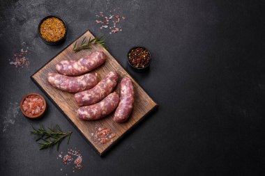 Koyu beton bir masada baharat ve otlarla ızgara yapılmış çiğ domuz sosisi. Evde yemek pişirmek.