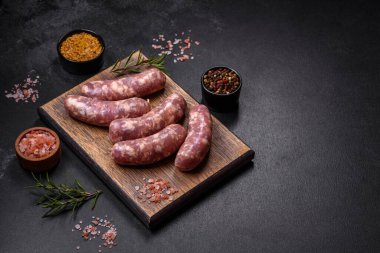 Koyu beton bir masada baharat ve otlarla ızgara yapılmış çiğ domuz sosisi. Evde yemek pişirmek.