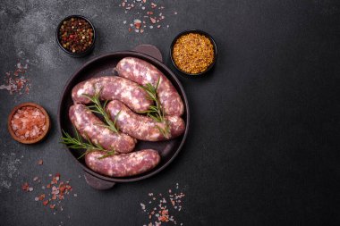 Koyu beton bir masada baharat ve otlarla ızgara yapılmış çiğ domuz sosisi. Evde yemek pişirmek.
