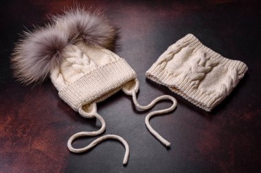 Koyu beton arka planda ponponlar olan güzel beyaz örülmüş kış şapkası. Soğuk kış giysileri.